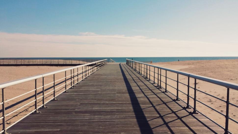 An empty coastal boardwalk stretching toward low hills under a soft morning sky